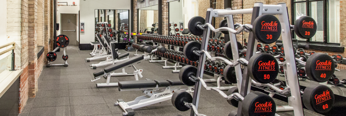 Weightlifting area in a GoodLife gym with barbells, dumbbells and lifting machines.